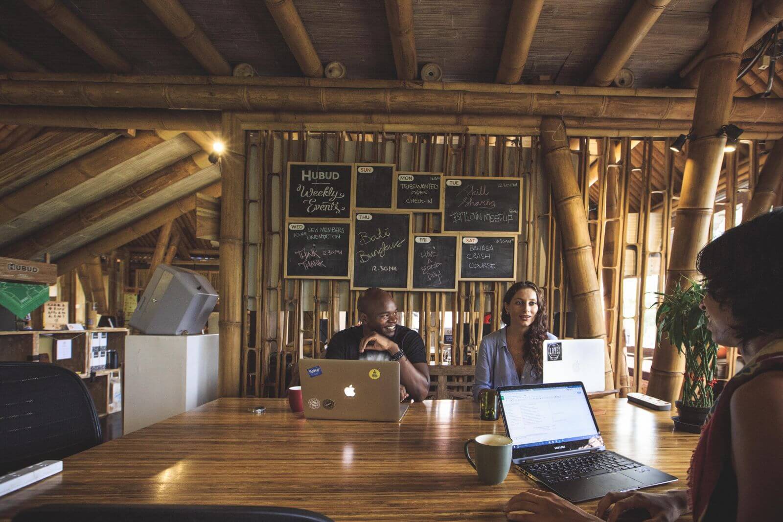 Terdapat 3 orang dengan laptop yang diletakkan di atas meja di sebuah ruangan yang memiliki furniture dari bambu